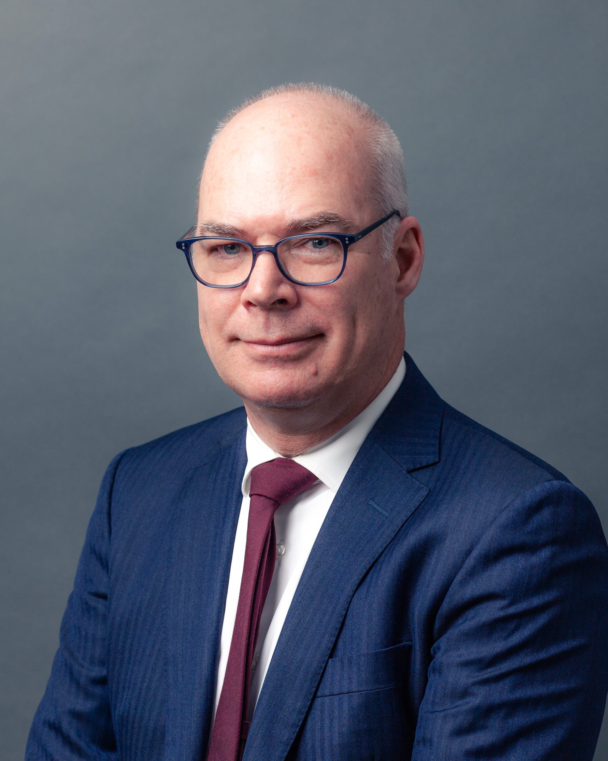 Headshot of lawyer Bruce Hutchison in blue suit on grey background